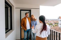 Un couple visite un logement et discute sur le balcon avec l'agent immobilier femme de dos. 