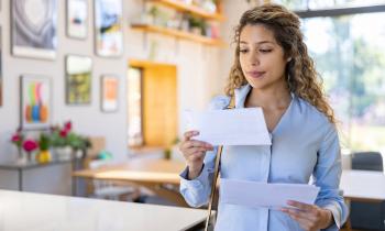Une jeune femme blonde aux cheveux bouclés lit une lettre qu'elle vient de recevoir, debout dans son salon