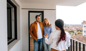 Un couple visite un logement et discute sur le balcon avec l'agent immobilier femme de dos. 