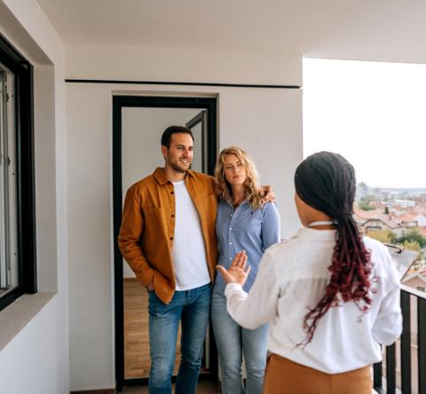 Un couple visite un logement et discute sur le balcon avec l'agent immobilier femme de dos. 